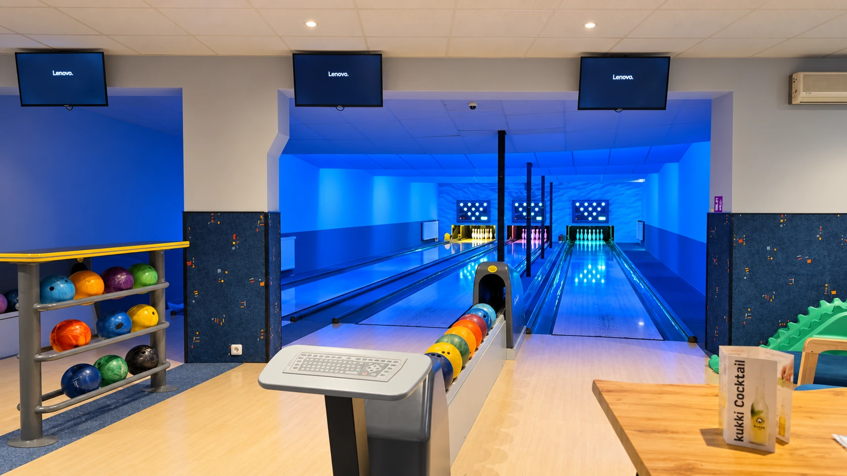Hauseigene Bowlingbahn im Hotel Hasa mit blauer Neonbeleuchtung, drei Bahnen und bunten Bowlingkugeln.