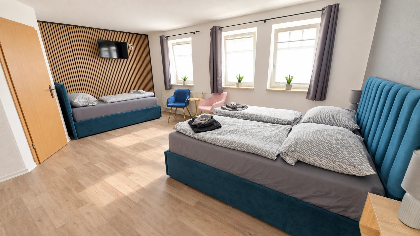 Dreibettzimmer im Hotel Hasa mit drei Betten, Holzlamellenwand und TV.