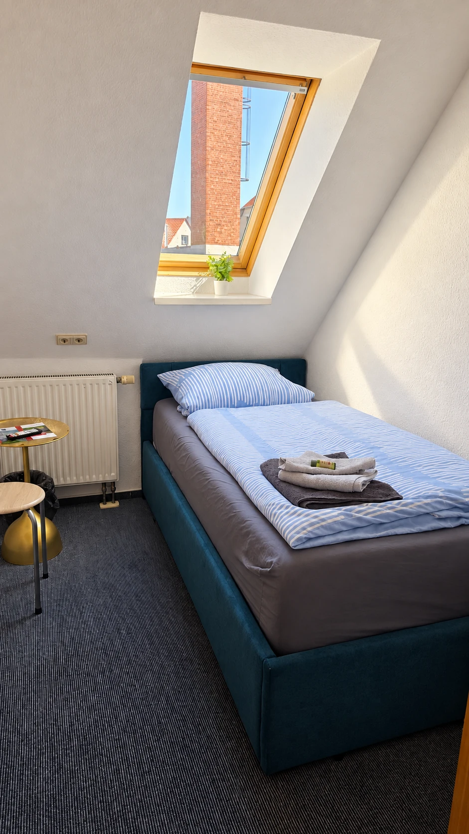 Einzelzimmer im Dachgeschoss des Hotel Hasa mit Dachschräge, Dachfenster und petrolfarbenem Bett.