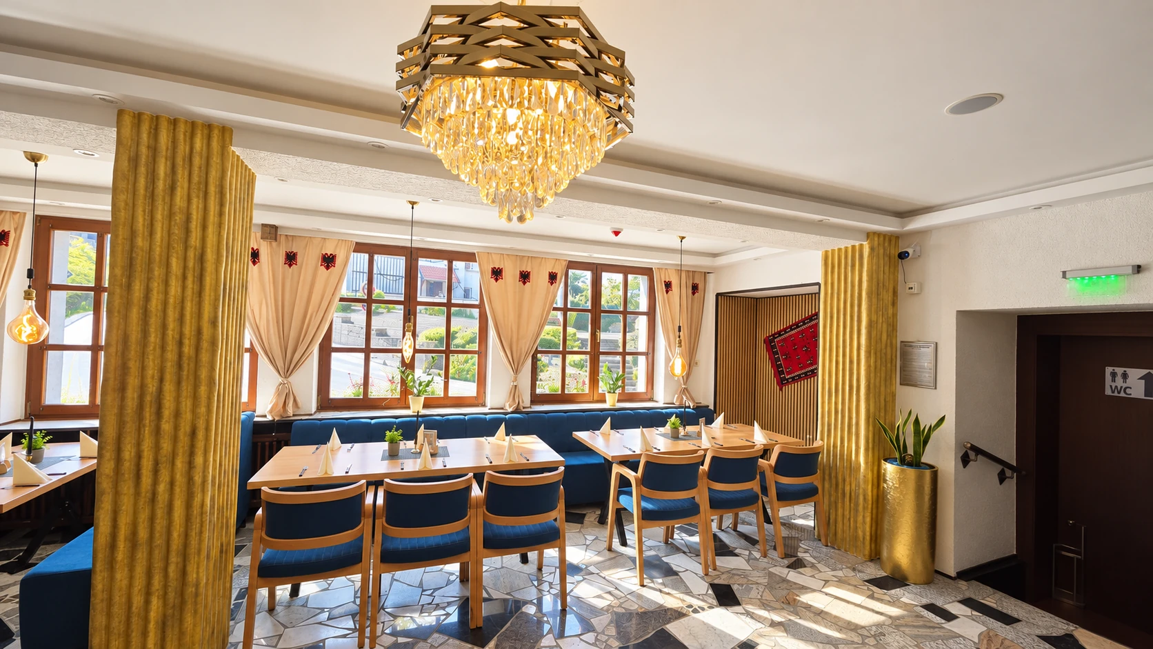 Gastraum des Restaurant Hasa mit goldenem Kronleuchter, albanisch bestickten Gardinen und Blick ins Grüne.
