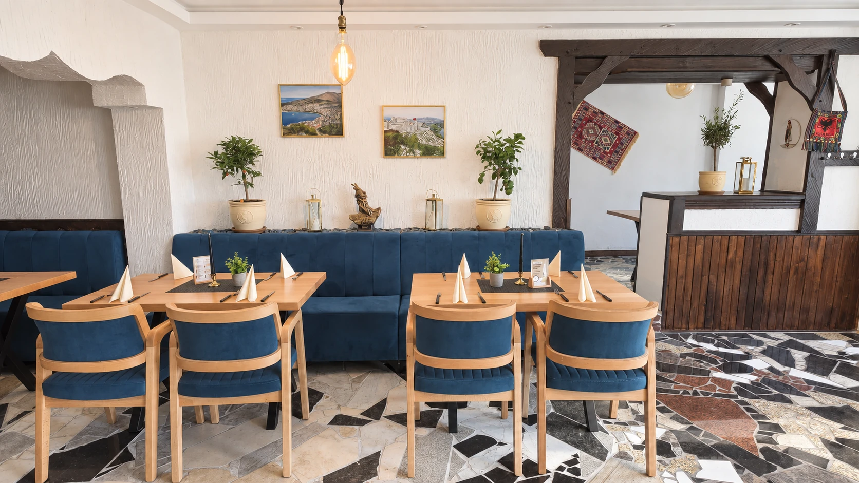 Empfangsbereich im Hotel Hasa mit Olivenbäumchen, albanischen Landschaftsbildern und Kelim-Teppich.